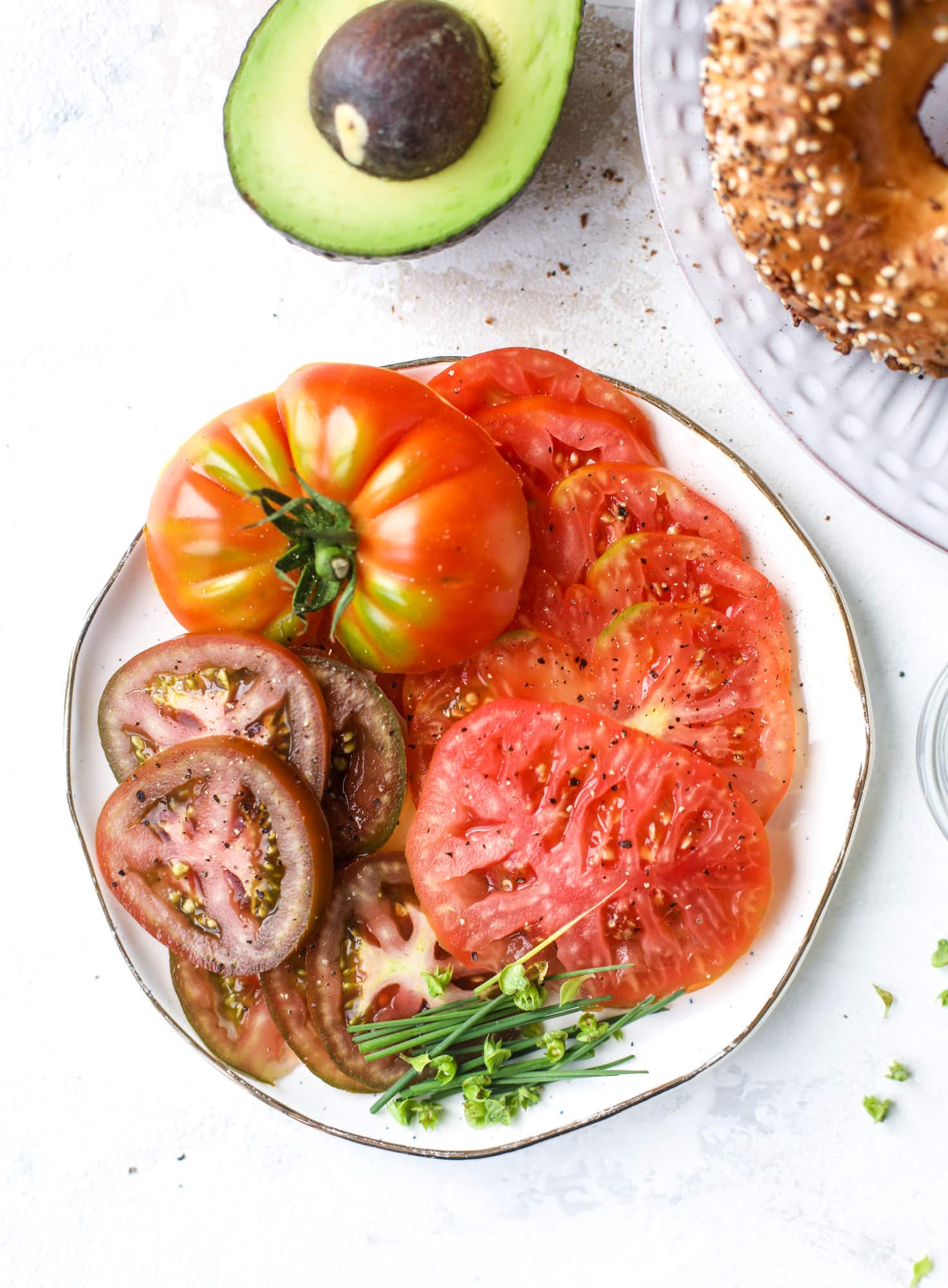 These avocado tomato sandwiches are the perfect lunch! Complete with veggie cream cheese, smoked sea salt, fresh chives and microgreens, the sliced avocado and heirloom tomatoes are sandwiched on an everything bagel for a flavor explosion. I howsweeteats.com #avocado #tomato #sandwich #healthy #lunch