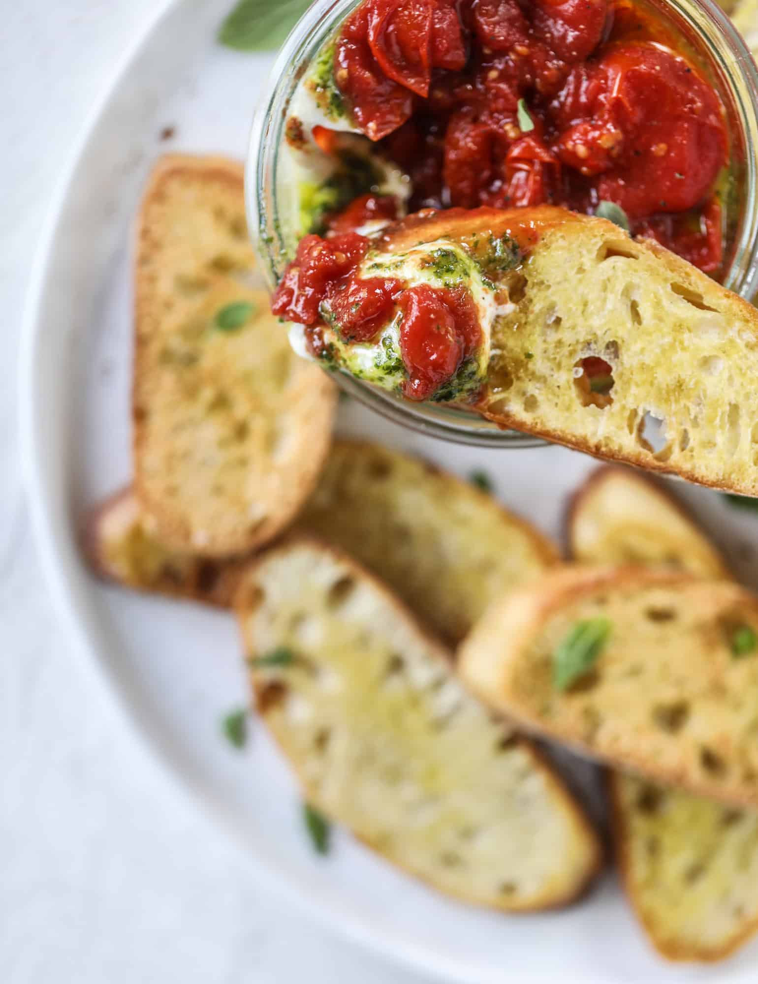 This ricotta jam jar is the perfect appetizer and snack to serve at a party! Based on the ricotta jam jar served at Nordstrom Cafe, it starts with creamy ricotta, is topped with flavorful basil pesto and a quick tomato jam. Serve with crunchy bread and dip dip dip! I howsweeteats.com #ricotta #jam #jar #nordstrom #tomato #pesto #appetizer #dip