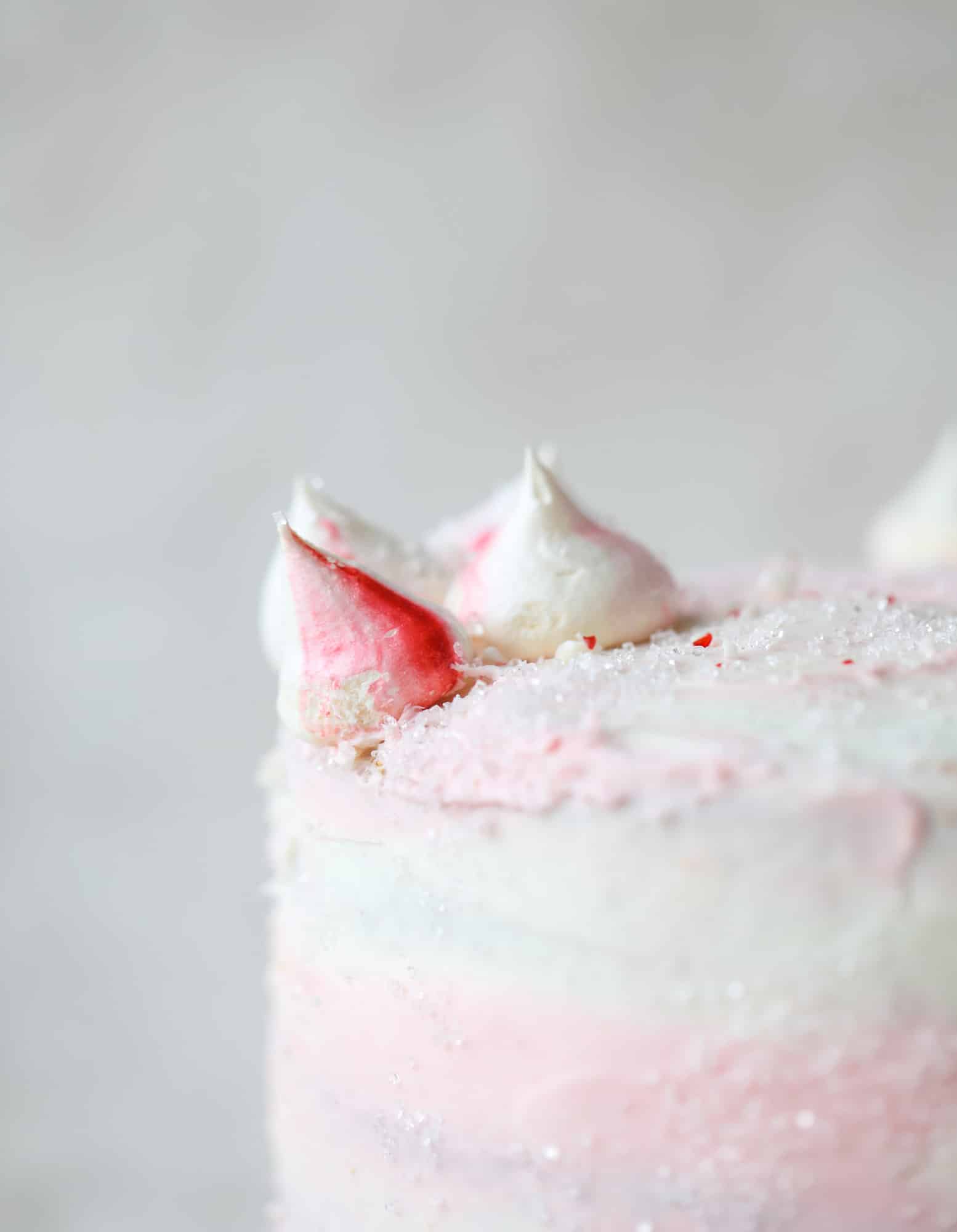 This pink peppermint cake is festive and delicious for the holidays! Layers of vanilla cake frosting with peppermint cream cheese frosting, covered in sparkly sugar and peppermint meringues. Couldn't be cuter! I #pinkpeppermint #cake