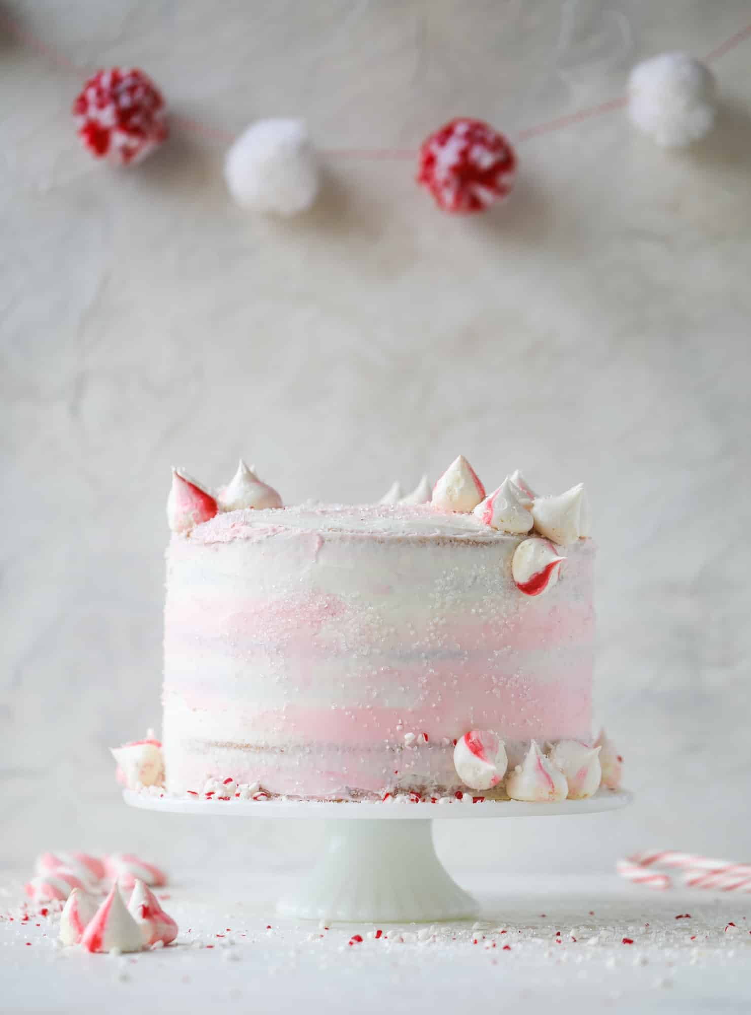 This pink peppermint cake is festive and delicious for the holidays! Layers of vanilla cake frosting with peppermint cream cheese frosting, covered in sparkly sugar and peppermint meringues. Couldn't be cuter! I #pinkpeppermint #cake