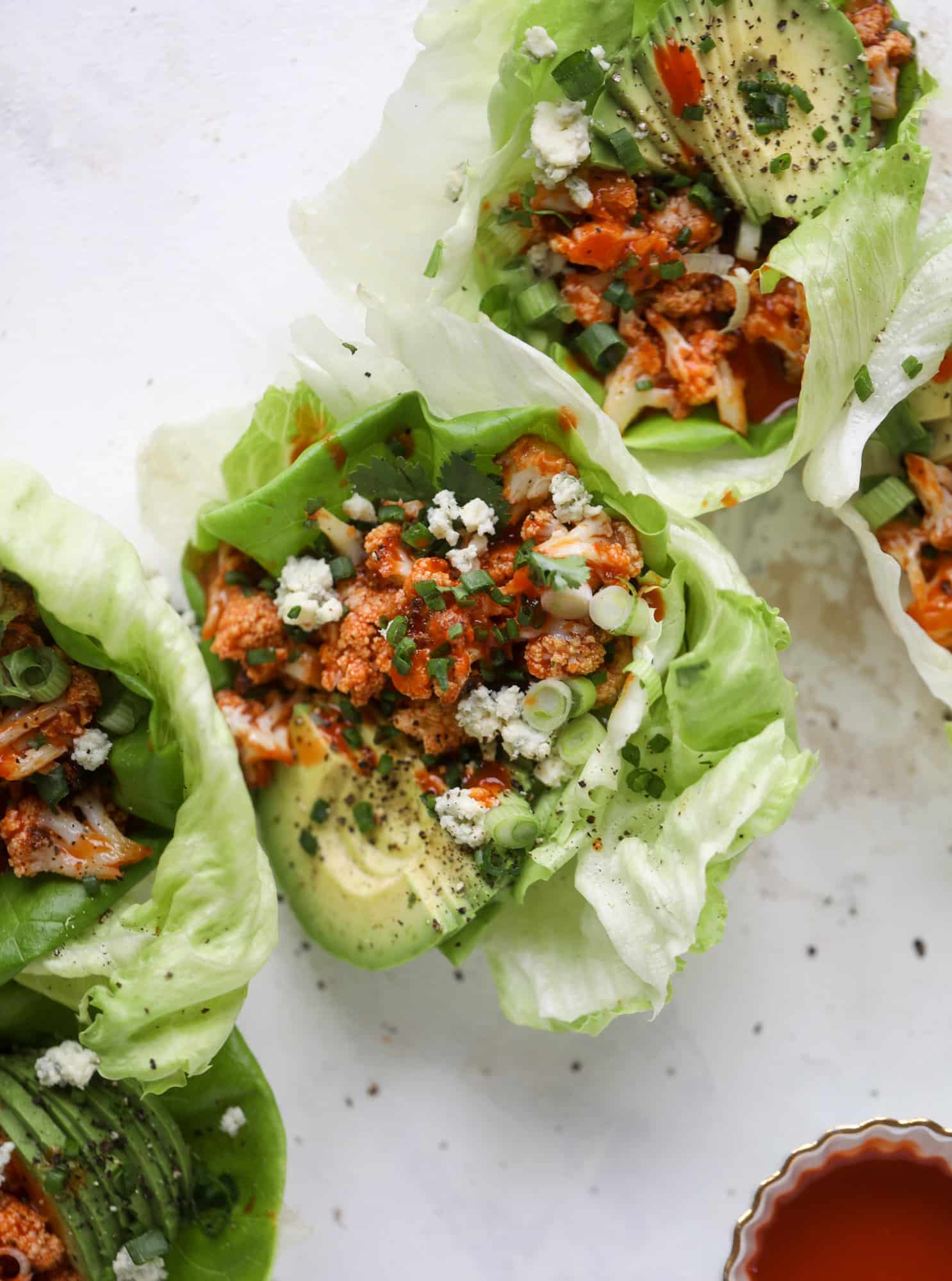 These buffalo cauliflower lettuce wraps are perfect for game day or even a quick weeknight dinner. Roasted cauliflower with buffalo wing sauce, sliced avocado, crumbled blue cheese, scallions, cilantro and chives makes for a flavor explosion! I howsweeteats.com #buffalo #cauliflower