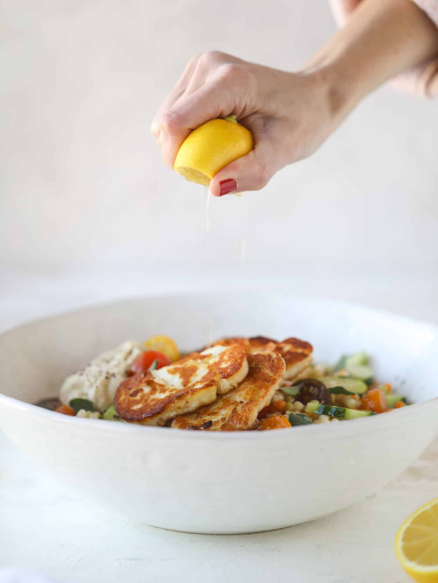 I am obsessed with these haulloumi hummus bowls for lunch or dinner. Couscous, veggies, crispy halloumi cheese and hummus with lots of lemon. Yum! I howsweeteats.com #halloumi #hummus