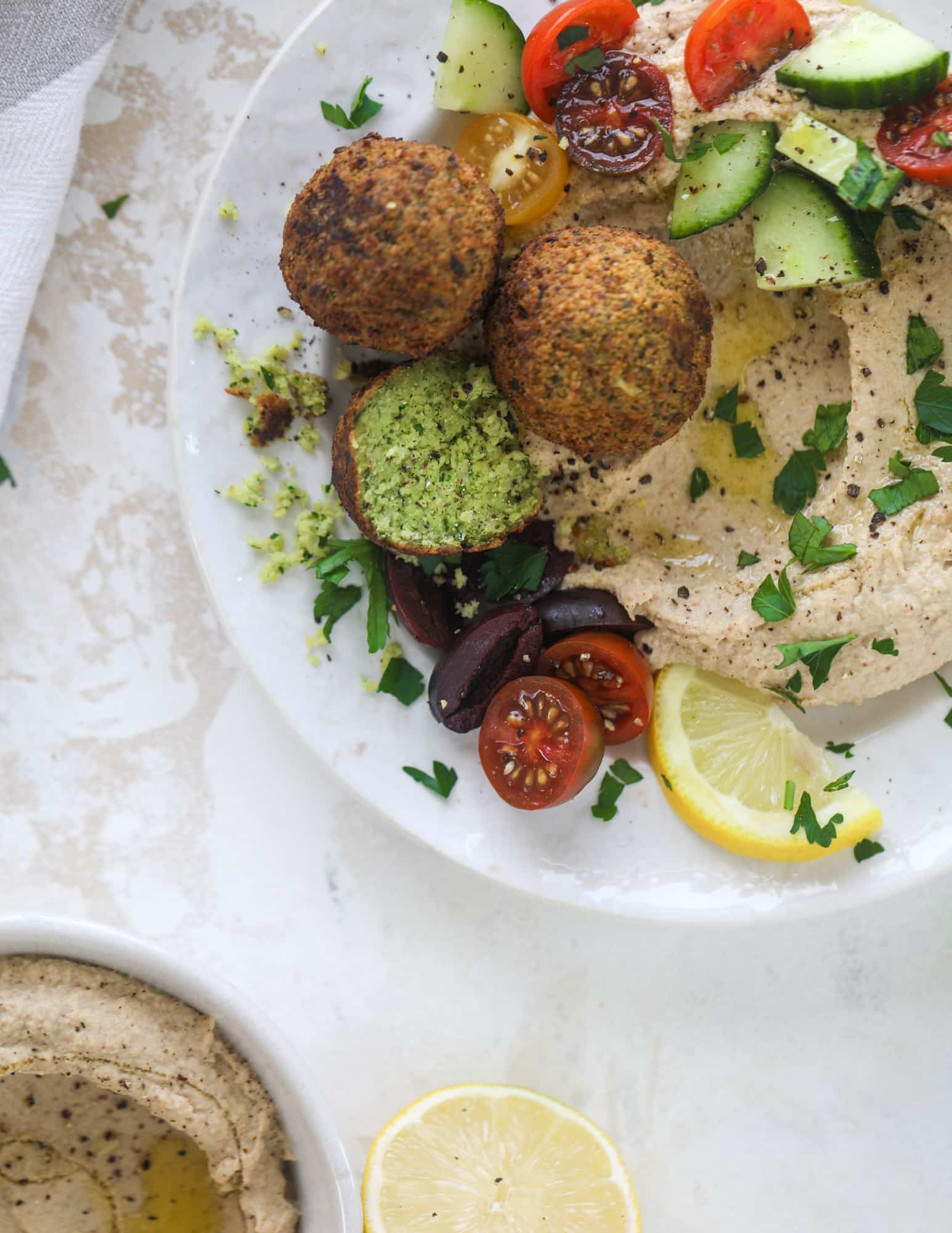 Green goddess falafel is hearty and flavorful, served over the creamiest cauliflower hummus, with tomatoes, olive, cucumbers and feta. Yum! I howsweeteats.com #falafel #cauliflowerhummus
