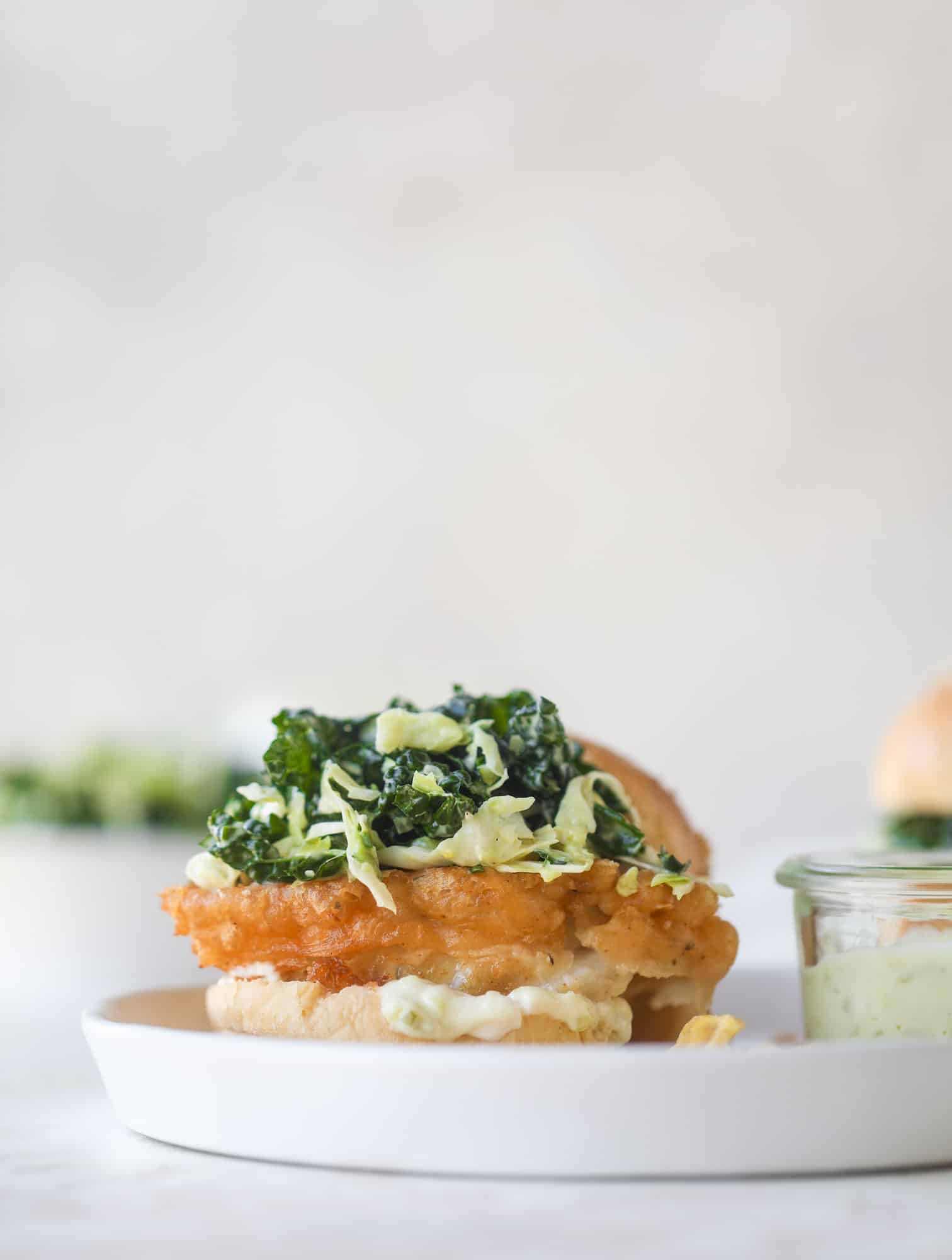 A light and crispy fish sandwich made with a simple beer batter and topped with a hearty, creamy kale cole slaw. Loaded with flavor! I howsweeteats.com #crispyfish #sandwich