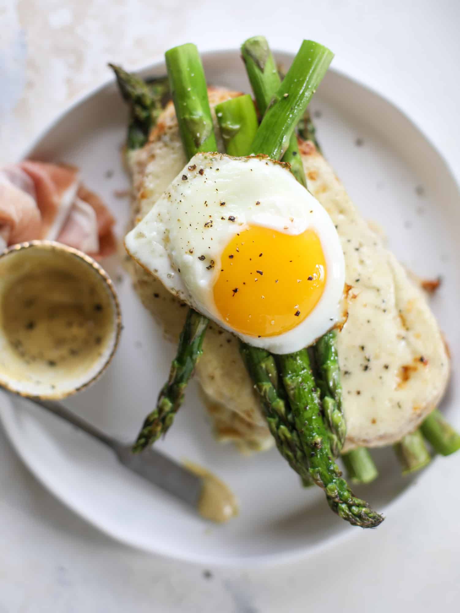 This roasted asparagus croque madame is made with thinly-sliced prosciutto and a fontina cheese sauce. Lots of dijon and an egg on top! I howsweeteats.com #croquemadame #asparagus