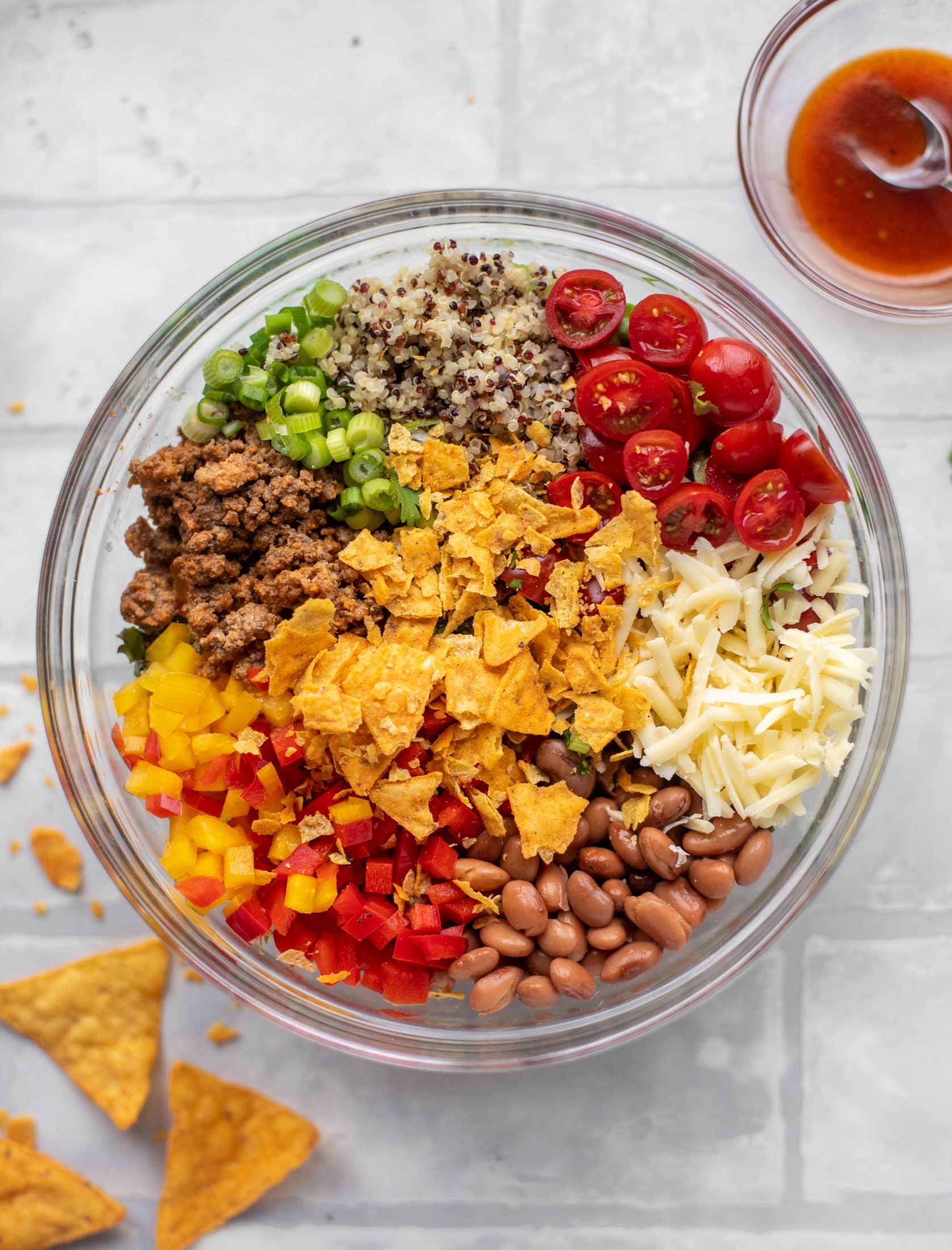 taco beef, scallions, quinoa, tomatoes, cheese, beans, peppers, chips in a bowl
