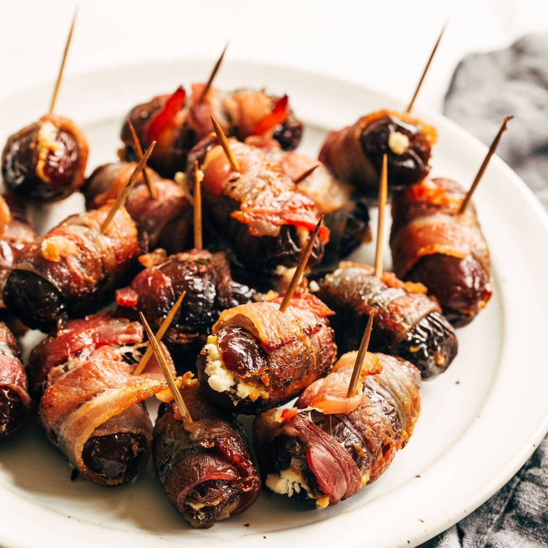 Bacon wrapped dates on a plate with toothpicks in the dates