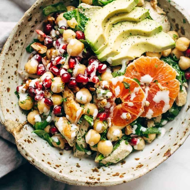 Spa salad in a bowl topped with chicken, avocado, and oranges.