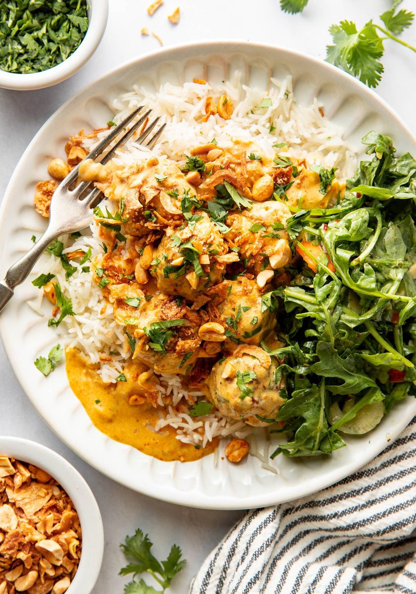 Yellow curry meatballs on a plate with rice and greens.
