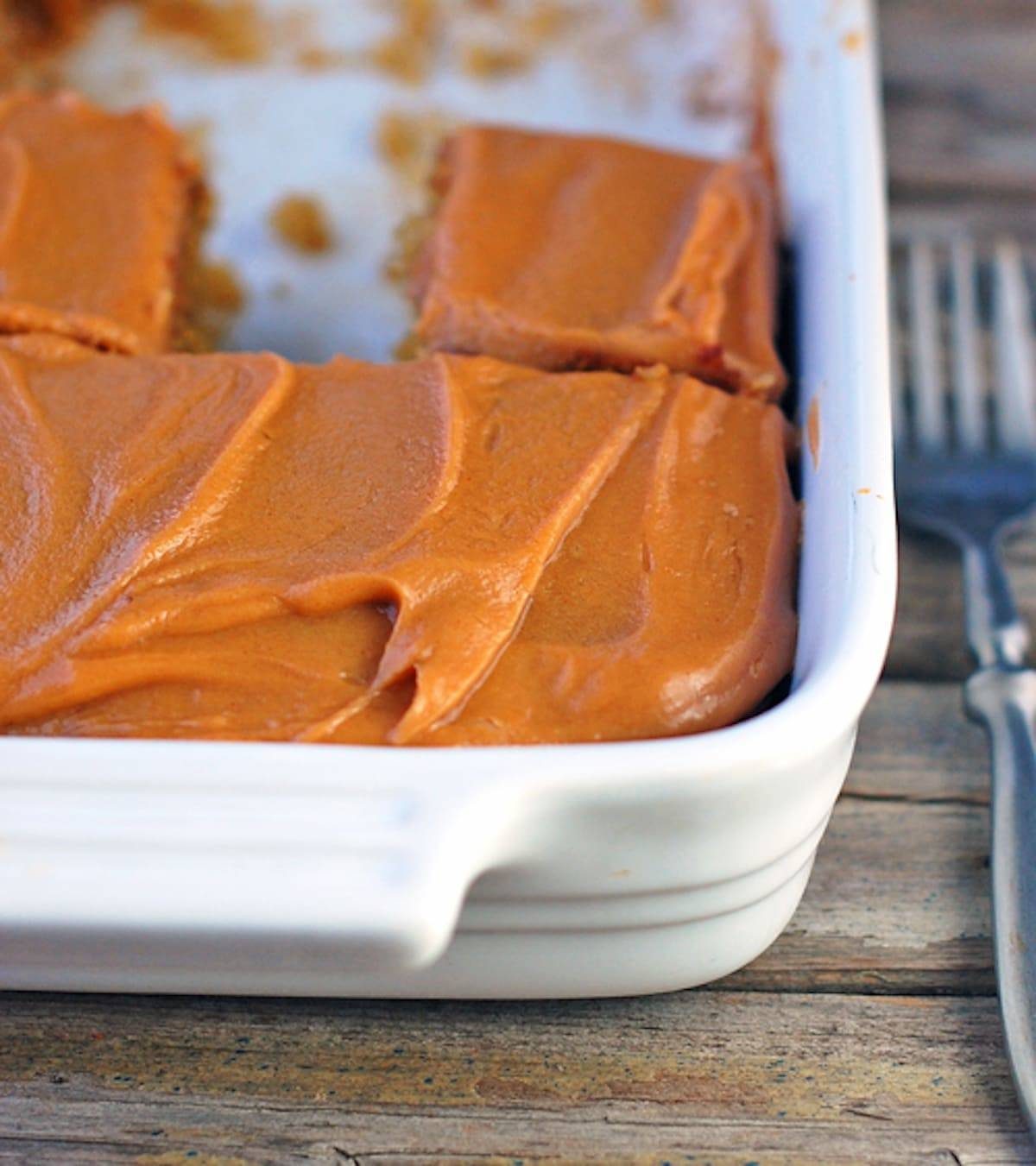 Banana cake with peanut butter frosting in a white baking dish on a wooden surface.