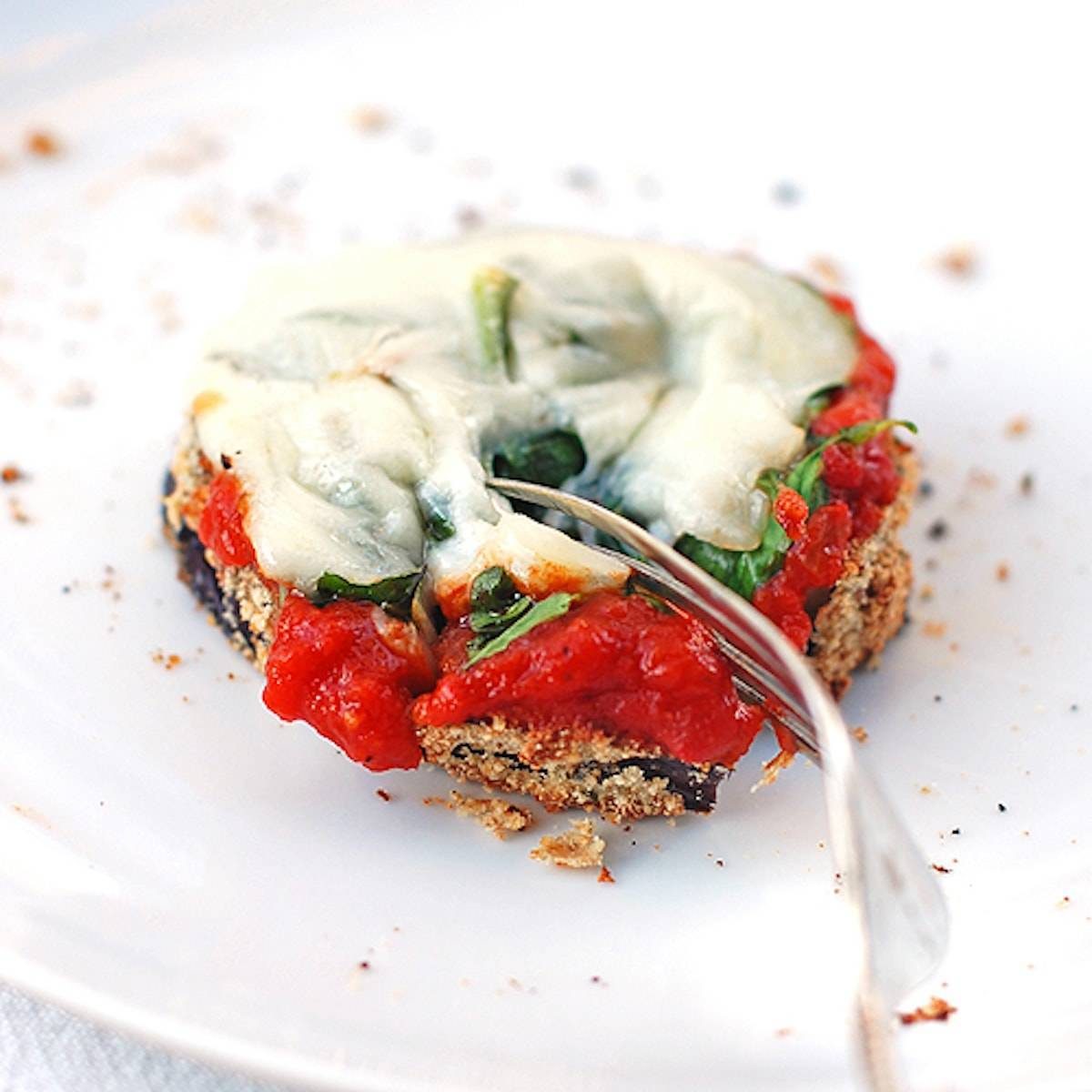 Eggplant pizza topped with marinara and melted cheese on a plate with a fork.