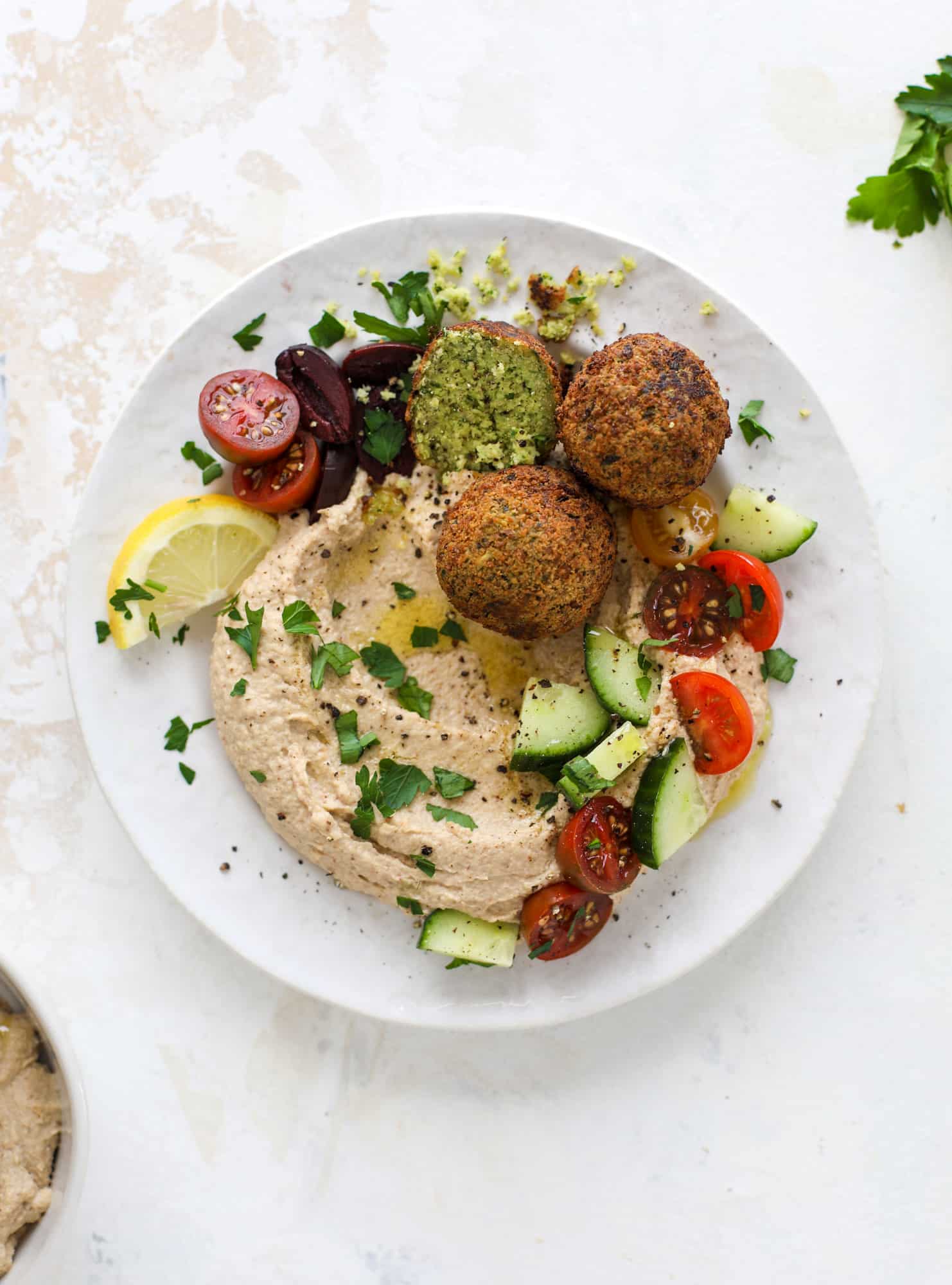 Green goddess falafel is hearty and flavorful, served over the creamiest cauliflower hummus, with tomatoes, olive, cucumbers and feta. Yum! I howsweeteats.com #falafel #cauliflowerhummus