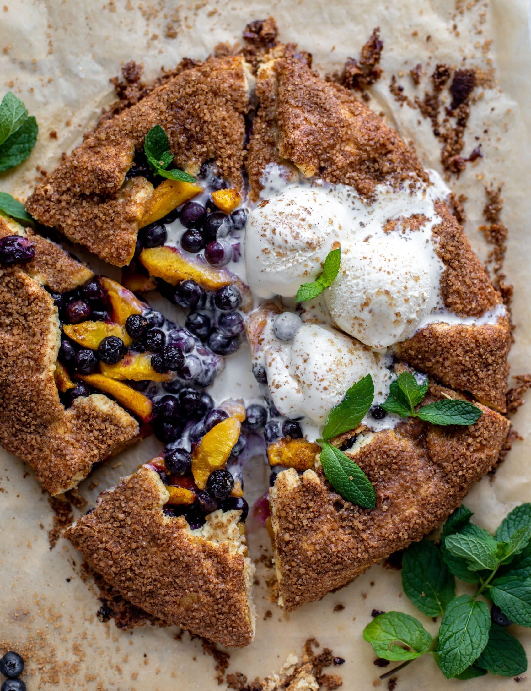 sliced blueberry peach galette with cinnamon sugar galette topped with ice cream and fresh mint