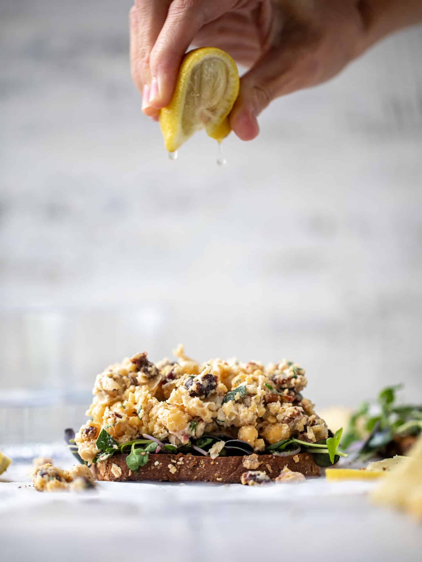 squeezing lemon on smashed chickpea salad on toast with micro greens